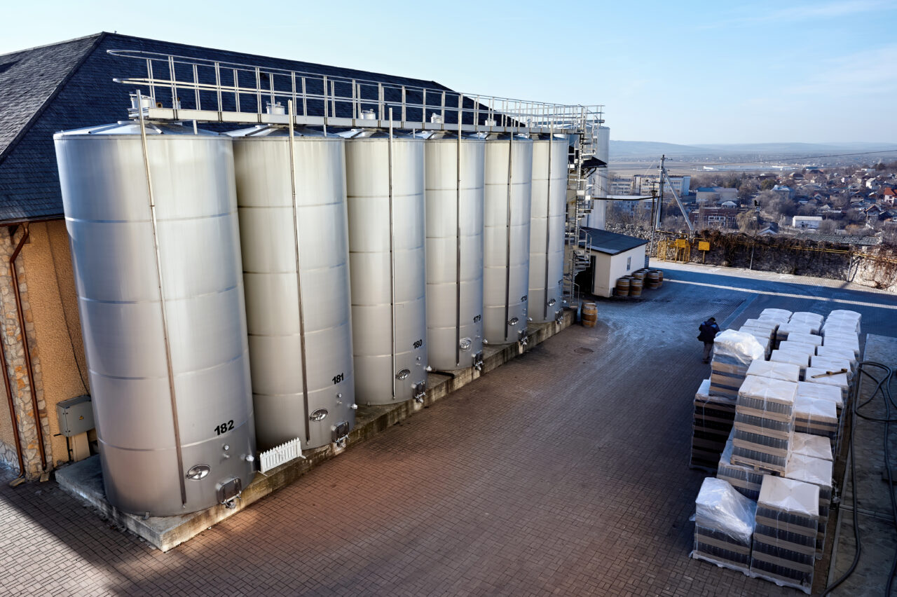 Metal wine storage tanks with dwelling houses on the background in a winery. Wide shot